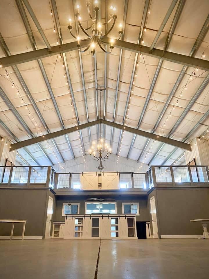 Open room with a vaulted beam ceiling, chandeliers, and a mezzanine across the far end.