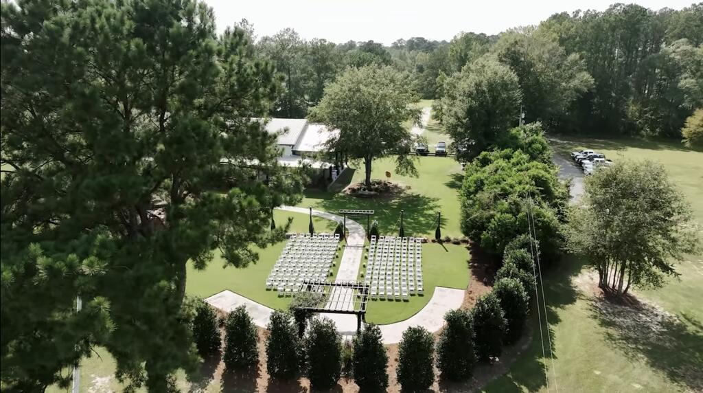 Landscaped event grounds with rows of ceremony chairs along a curved aisle beside a building.