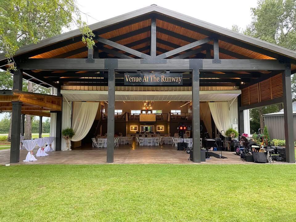 Open-sided event pavilion with a peaked timber roof and reception tables, signed Venue At The Runway.