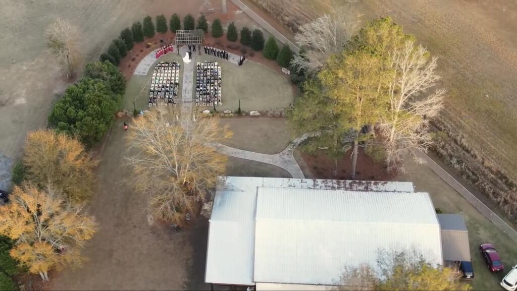 Aerial view of a metal-roofed building beside rows of outdoor chairs and a landscaped walkway.