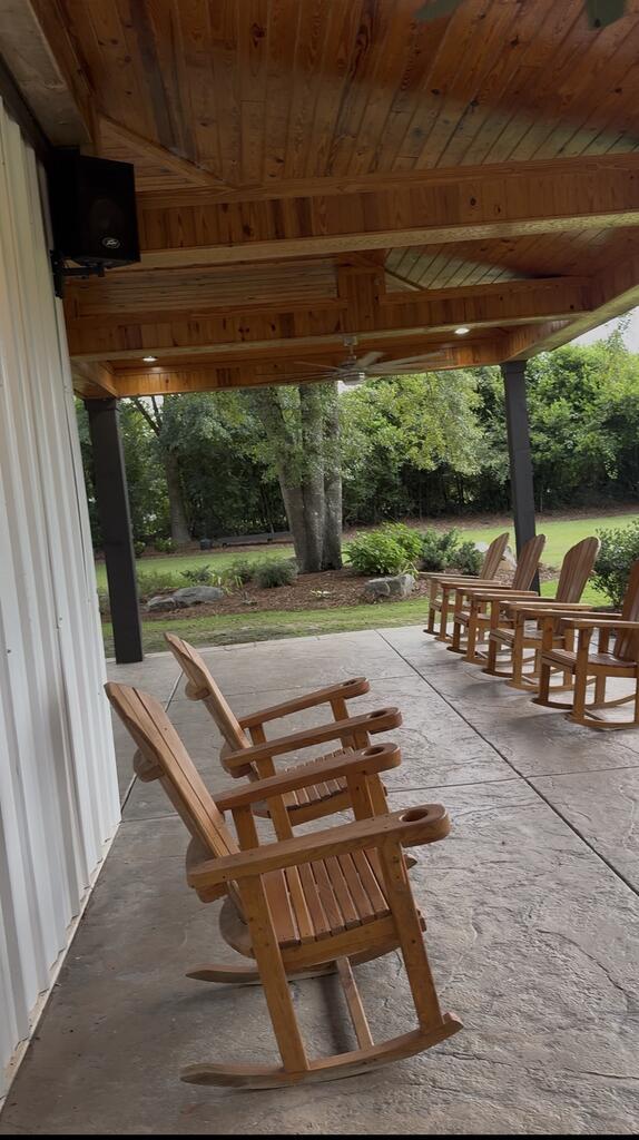 Covered patio with a wood-plank ceiling and wooden rocking chairs overlooking a leafy yard.