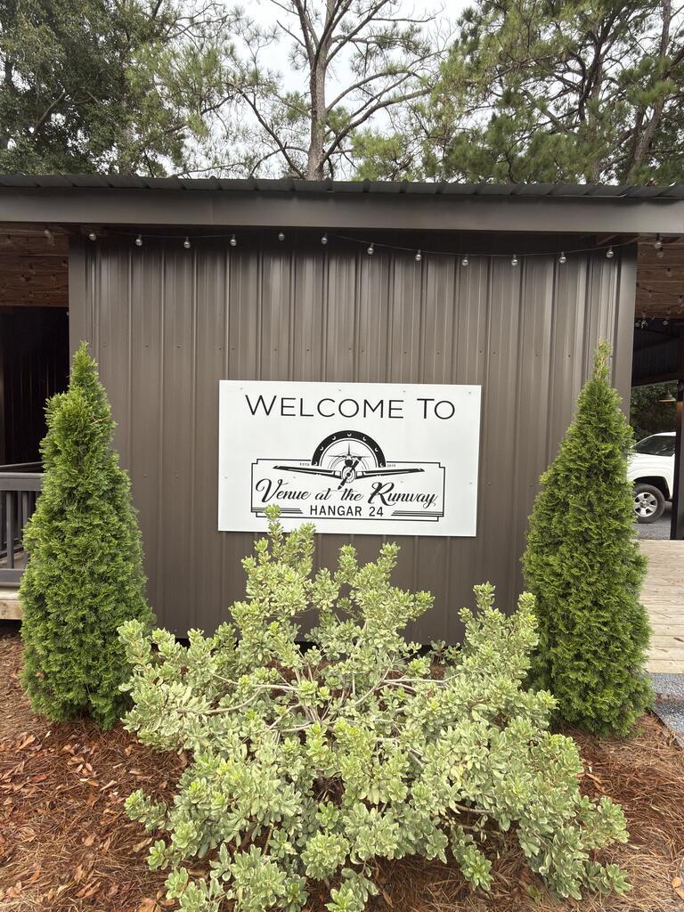 Venue at the Runway, Hangar 24 entrance sign framed by shrubs and string lights.