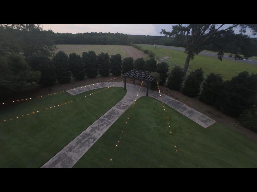Aerial view of a landscaped lawn with a lit pergola and branching concrete walkways at dusk.
