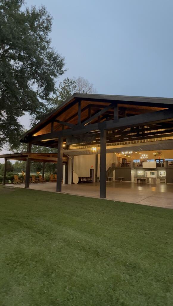Open-sided building with an exposed timber-truss roof and warmly lit interior at dusk.