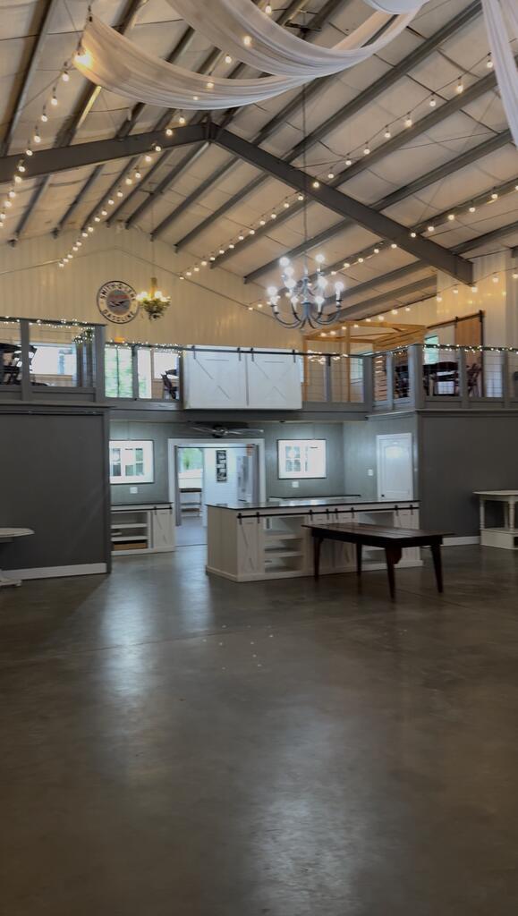 Spacious event venue with a mezzanine, draped ceiling, string lights, and chandeliers.