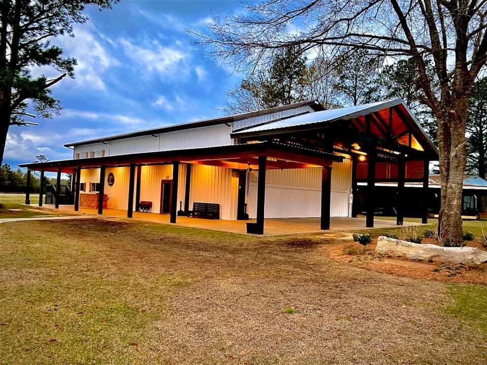 Light-colored metal building with a broad covered porch and warm lights glowing at dusk.