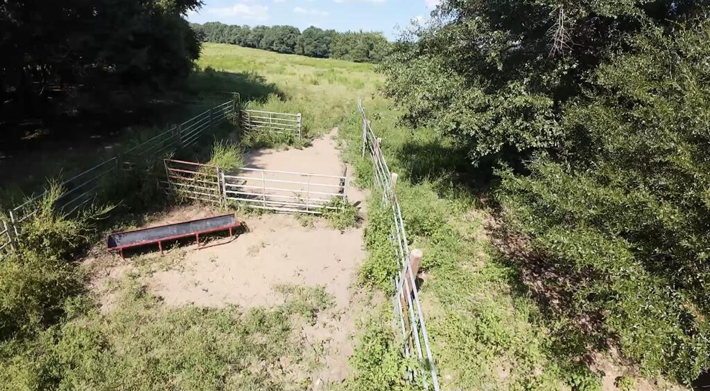 Aerial view of a fenced livestock pen with metal gates and a trough beside open pasture.