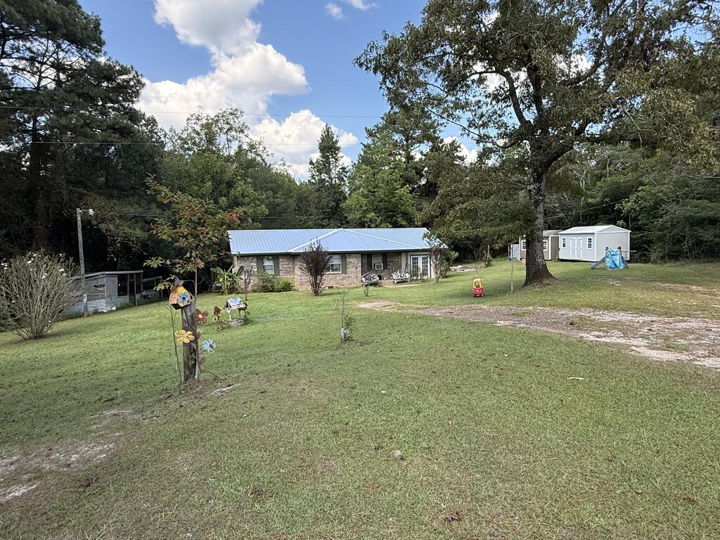 Brick ranch house with a metal roof in a spacious, tree-shaded grassy yard.