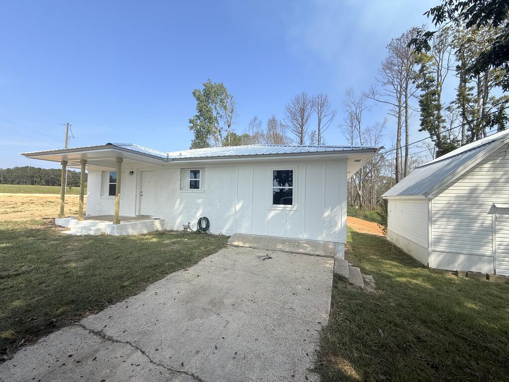 White single-story house with a covered porch, concrete driveway, and detached outbuilding.