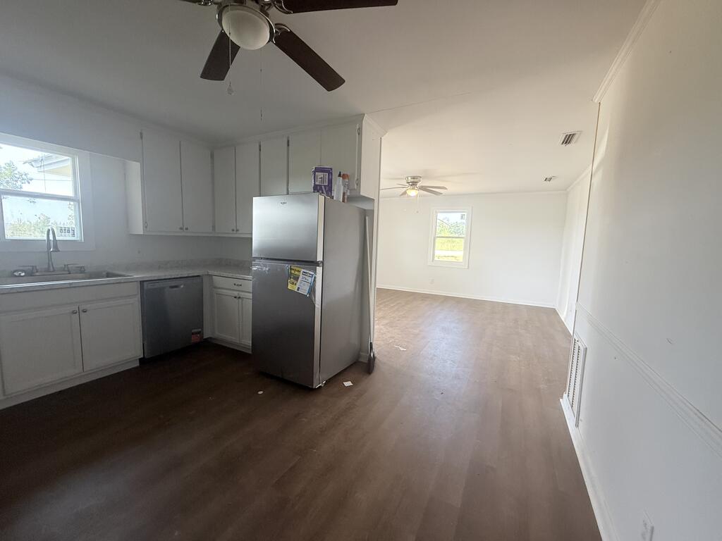 Unfurnished kitchen with white cabinets and stainless-steel appliances opening into a spacious adjoining room.