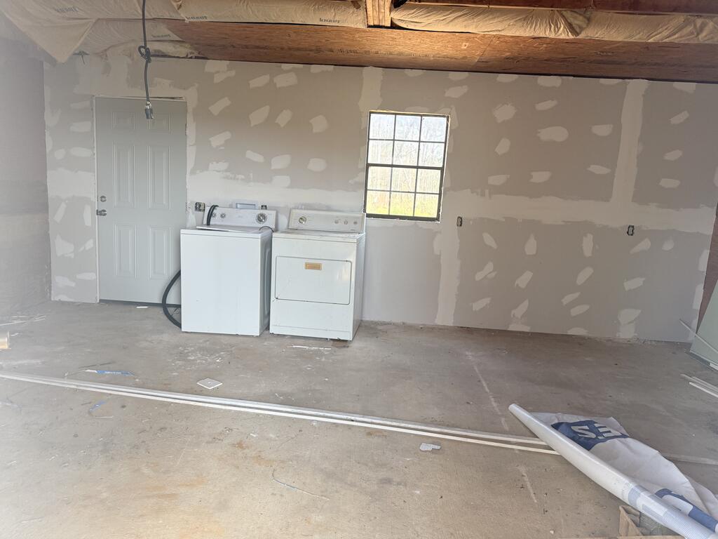 Unfinished laundry area with a white washer and dryer, patchy drywall, exposed beams, and concrete floor.