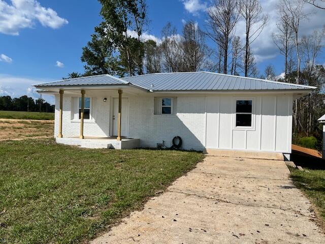 White single-story house with a gray metal roof, covered porch, and concrete driveway.