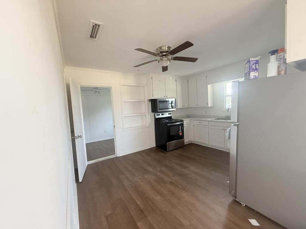 Kitchen with white cabinets, black range and microwave, and dark wood-look flooring.