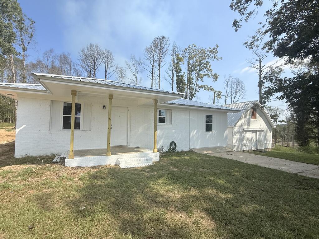 White single-story house with a covered porch, metal roof, and small outbuilding beside the driveway.