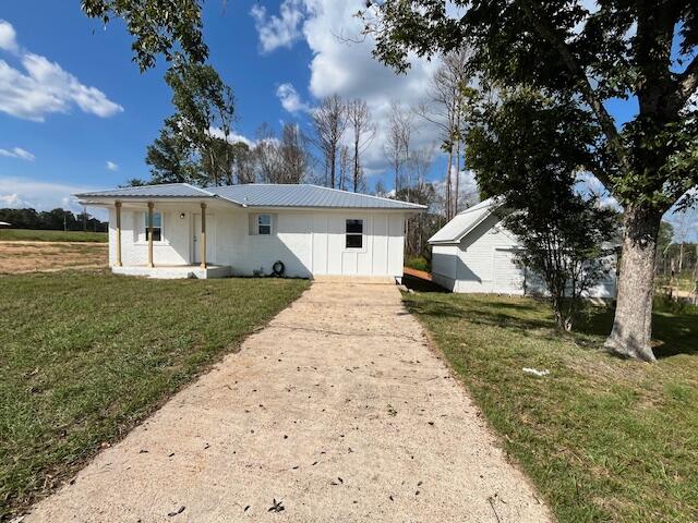 Small white building at the end of a concrete driveway, with a separate outbuilding and large tree.