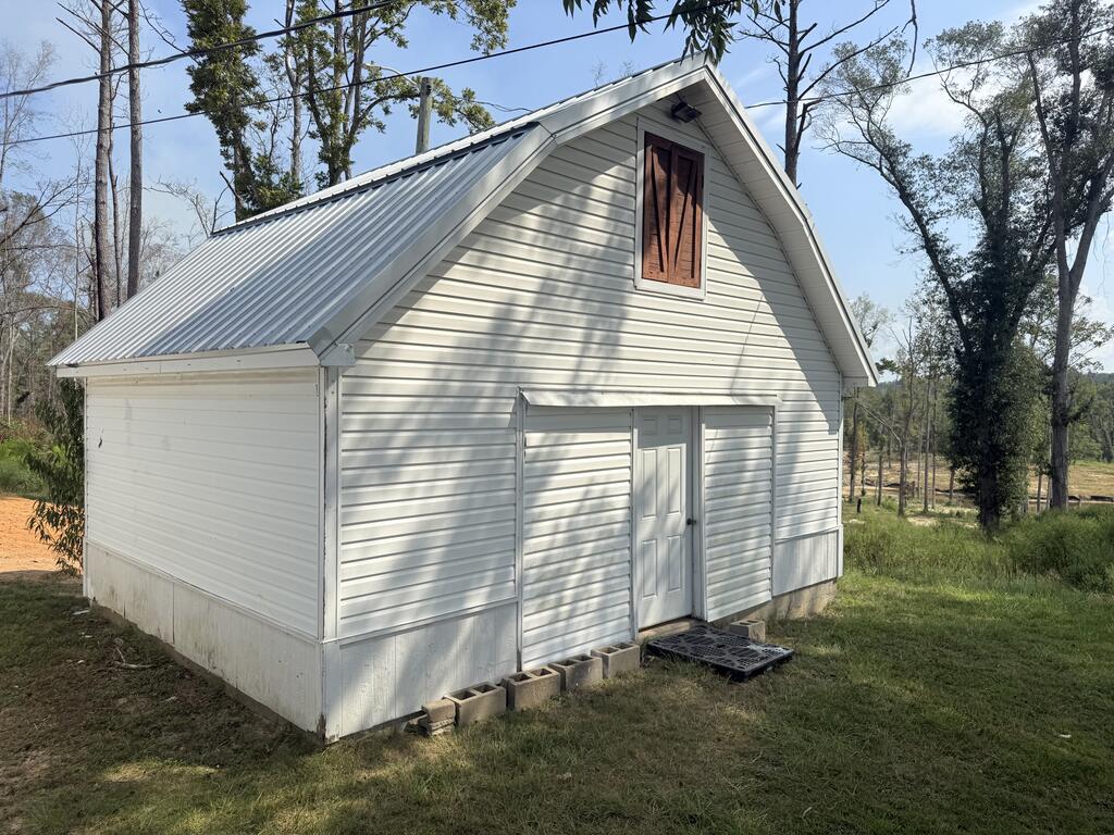 White outbuilding with a steep metal roof and wooden loft door among trees.