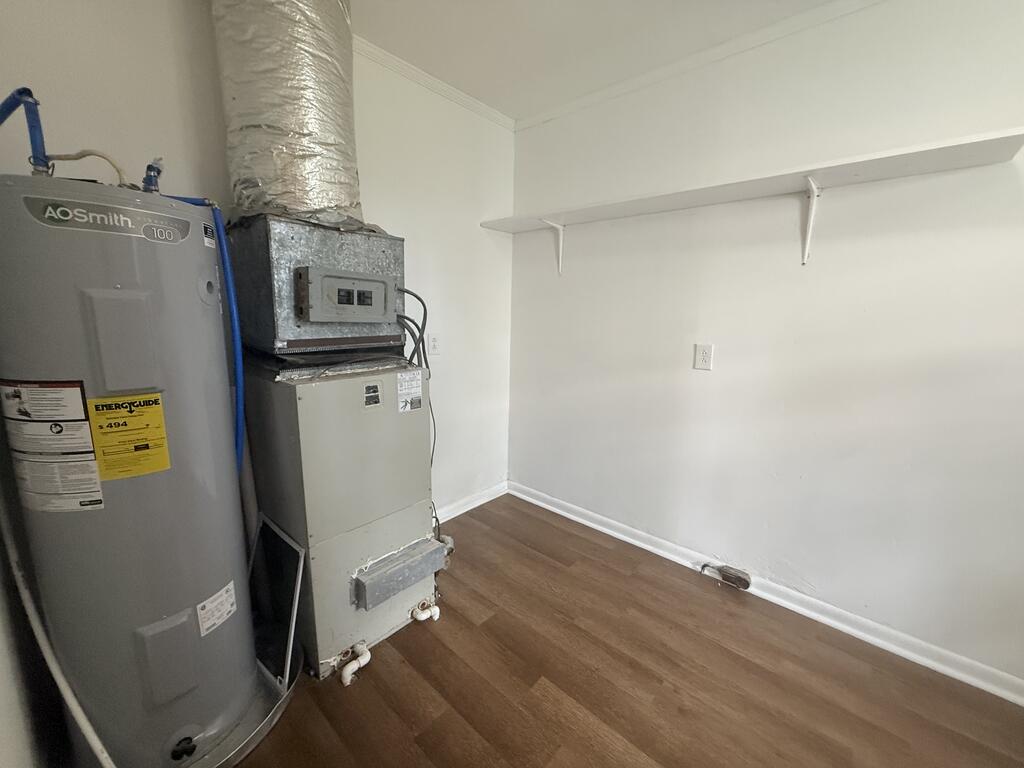 Utility room with a water heater, furnace, exposed ductwork, and a wall-mounted shelf.