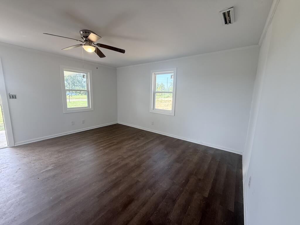 Empty room with dark wood-look flooring, two windows, and a ceiling fan.