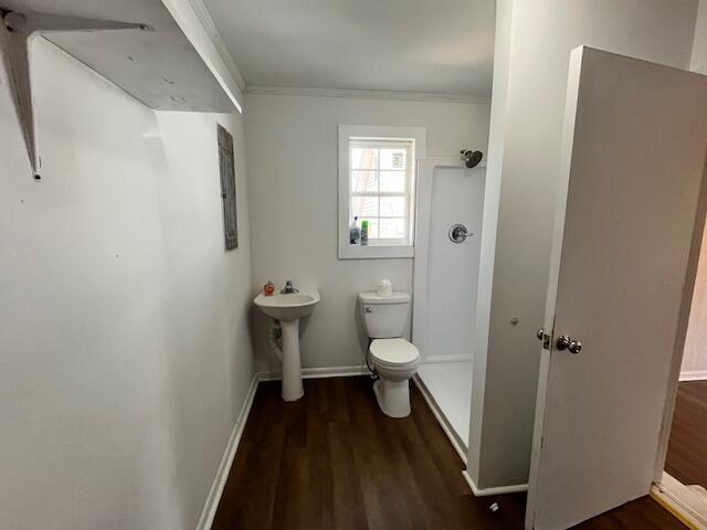Bathroom with a pedestal sink, toilet, shower, and dark wood-look flooring.