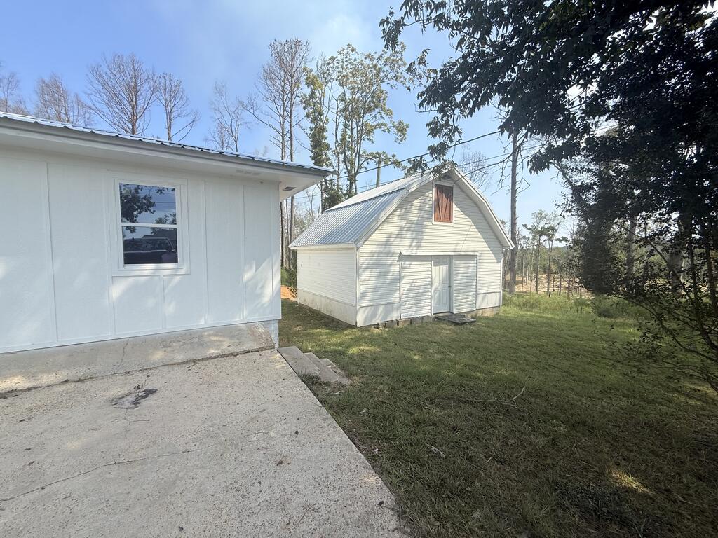 Two white outbuildings on a grassy lot, including a barn-style structure with a metal roof.