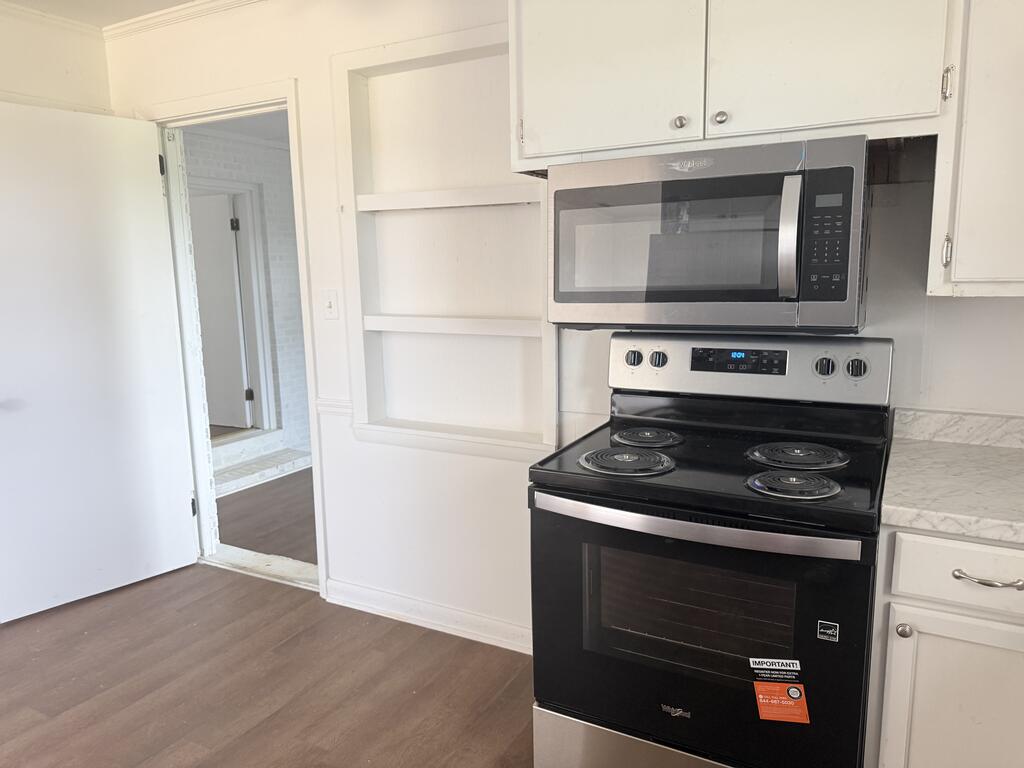 Kitchen with white cabinets, open shelves, and a black electric range beneath a stainless steel microwave.