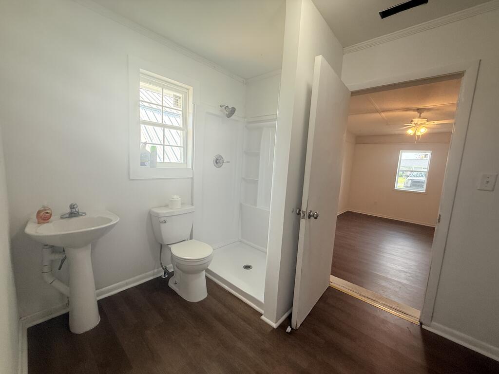 Bathroom with a pedestal sink, toilet, and shower stall opening to an empty room.