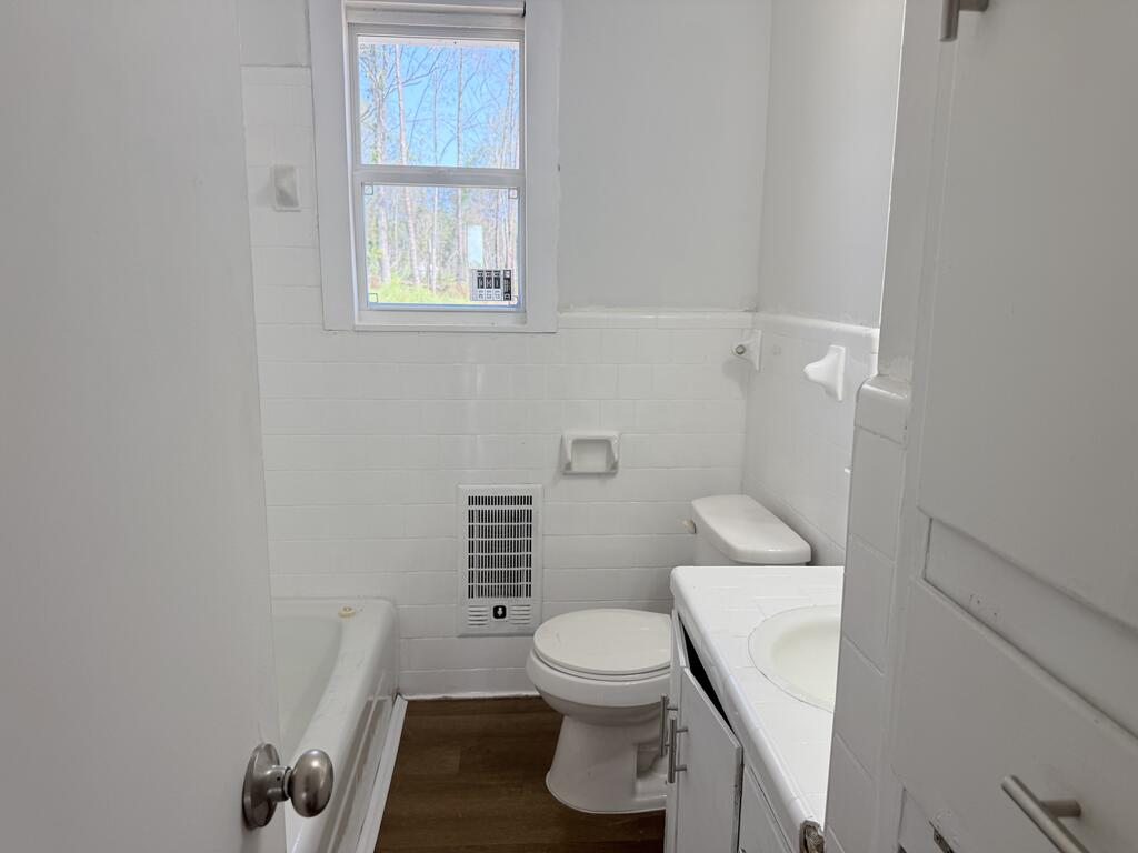 Bathroom with a bathtub, toilet, and white vanity beneath a window.