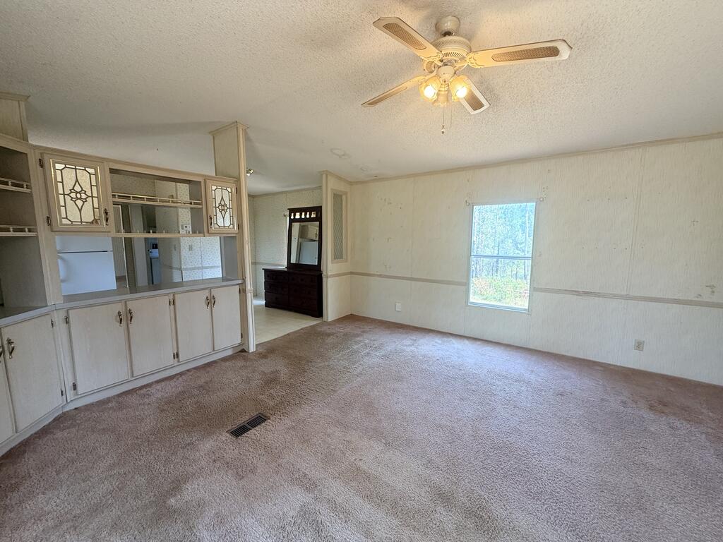 Empty carpeted room with built-in cabinets, a ceiling fan, and a window overlooking trees.