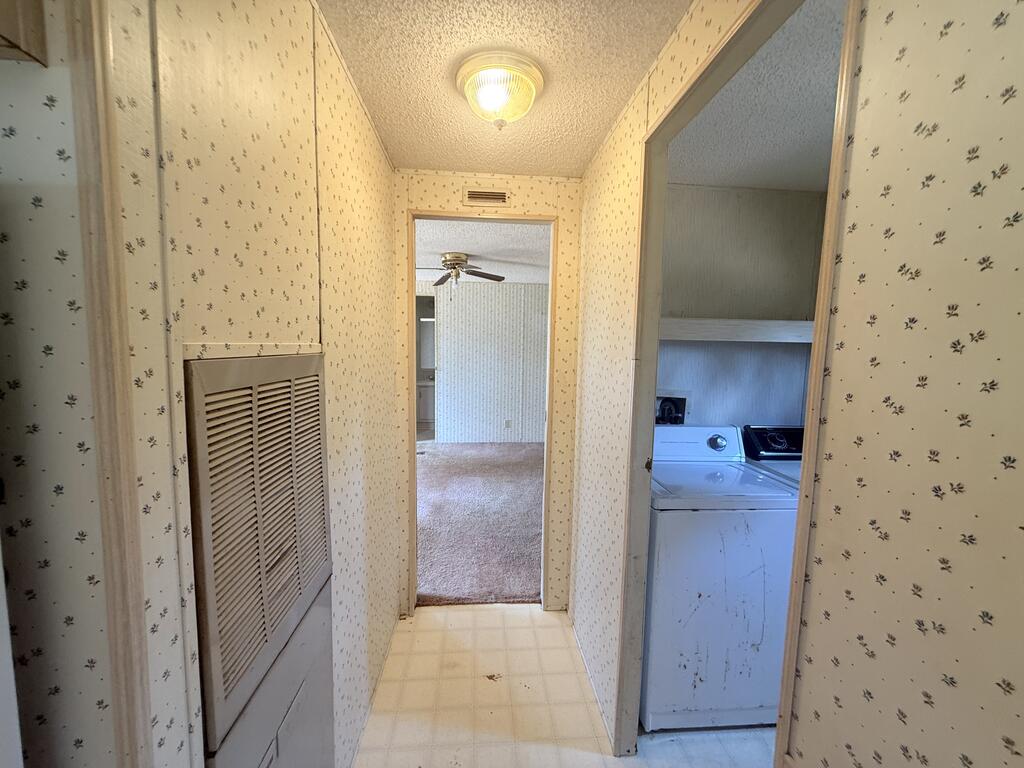 Hallway with patterned wallpaper, tiled floor, and an open doorway to a washer and dryer.