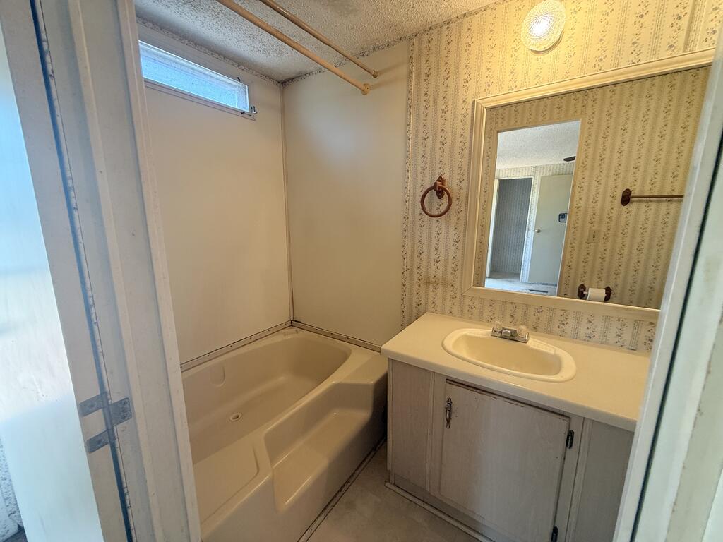 Bathroom with a bathtub, single-sink vanity, large mirror, and patterned wallpaper.