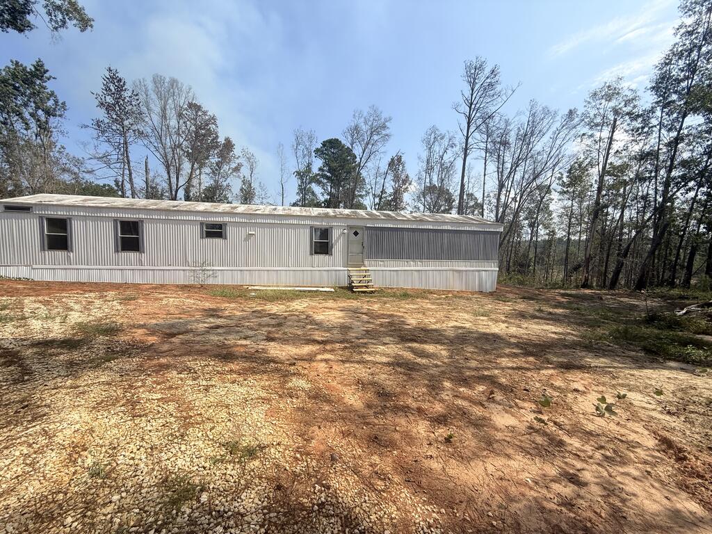 Manufactured home with light metal siding and front steps in a wooded clearing.