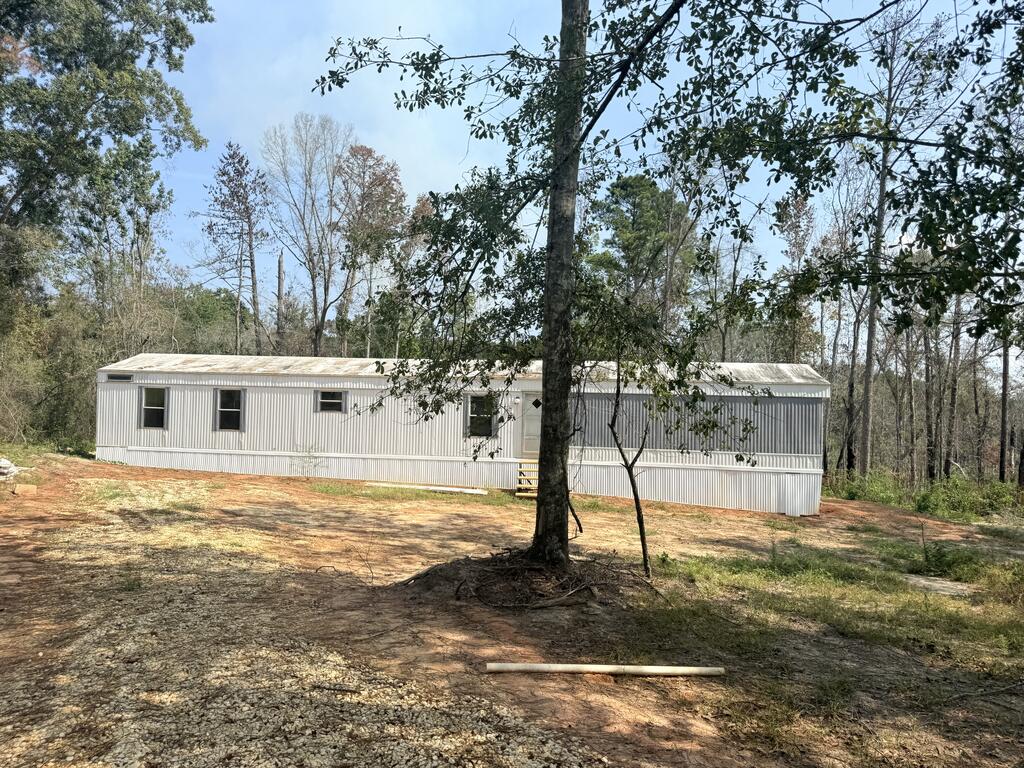 Long white manufactured home on a cleared, wooded lot.