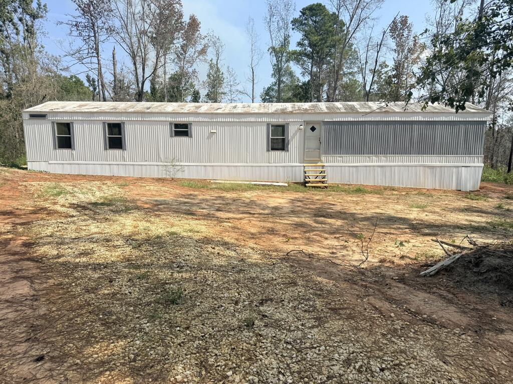 Long light-colored manufactured home with front steps and a raised platform in a cleared yard.