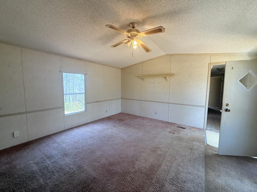Empty carpeted room with paneled walls, a ceiling fan, and a window.