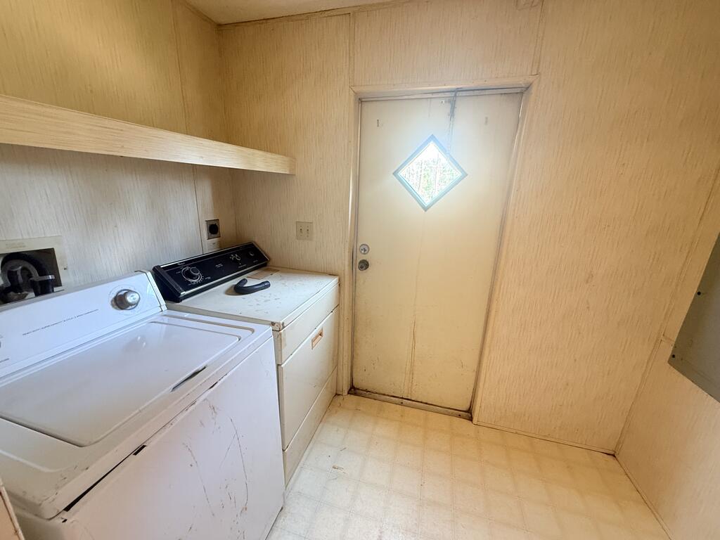Laundry room with a white washer and dryer beside a door with a diamond-shaped window.