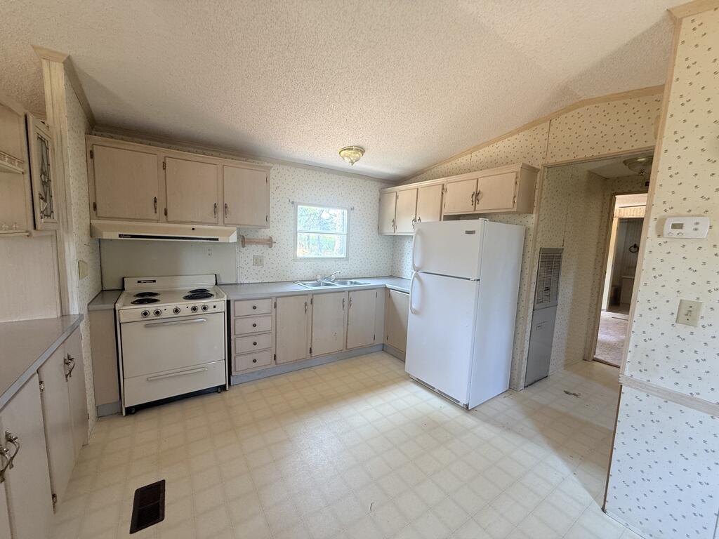 Kitchen with cream cabinets, white appliances, and patterned wallpaper.