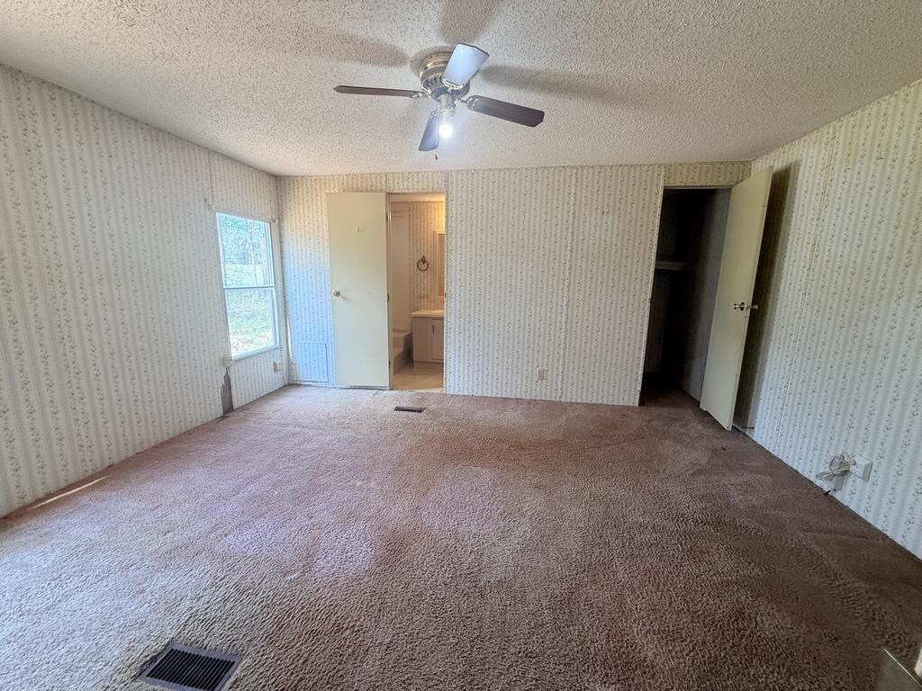 Empty bedroom with patterned wallpaper, brown carpet, and doors to a bathroom and closet.