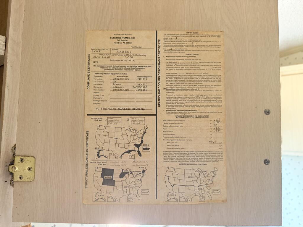 Manufactured home certification label with compliance details and design-zone maps on a wood cabinet door.