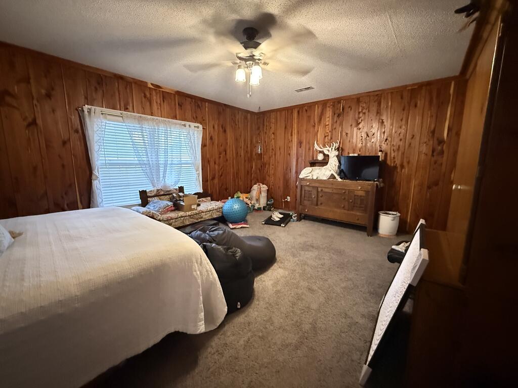 Bedroom with wood-paneled walls, beige carpet, and a ceiling fan.