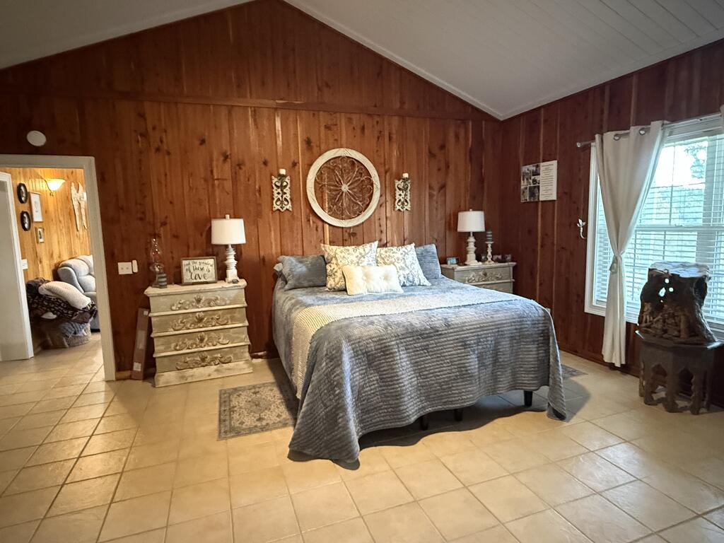 Furnished bedroom with a large bed, wood-paneled walls, and a vaulted ceiling.