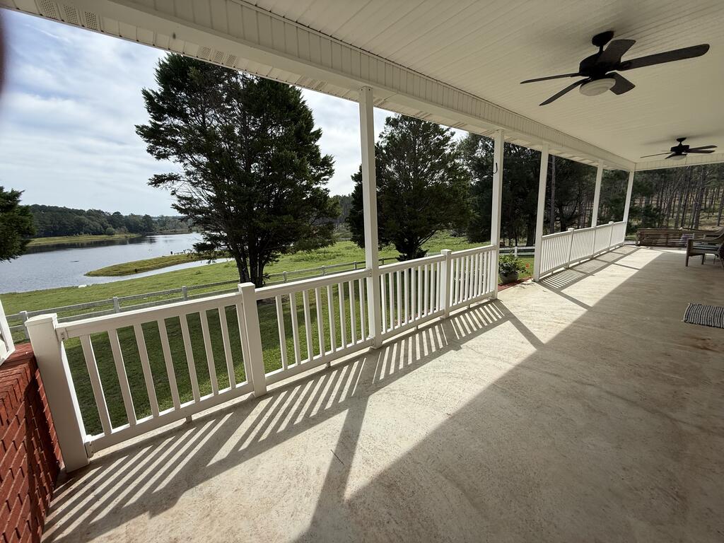 Covered porch overlooking a pond, with white railings and ceiling fans.