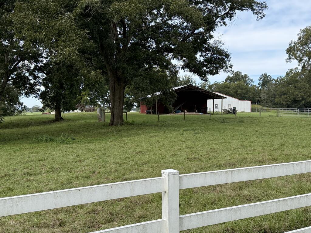 Fenced grassy pasture with mature trees and a metal barn in the distance.