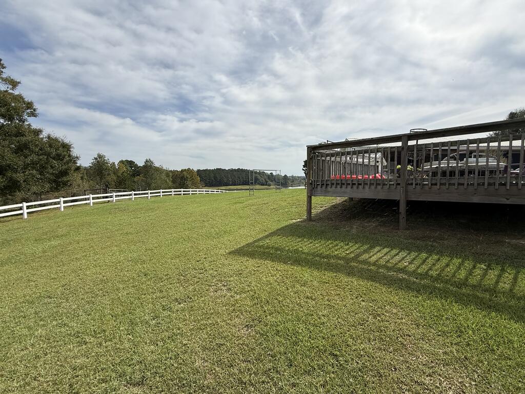 Wide lawn with a raised wooden deck and long white fence under a cloudy sky.