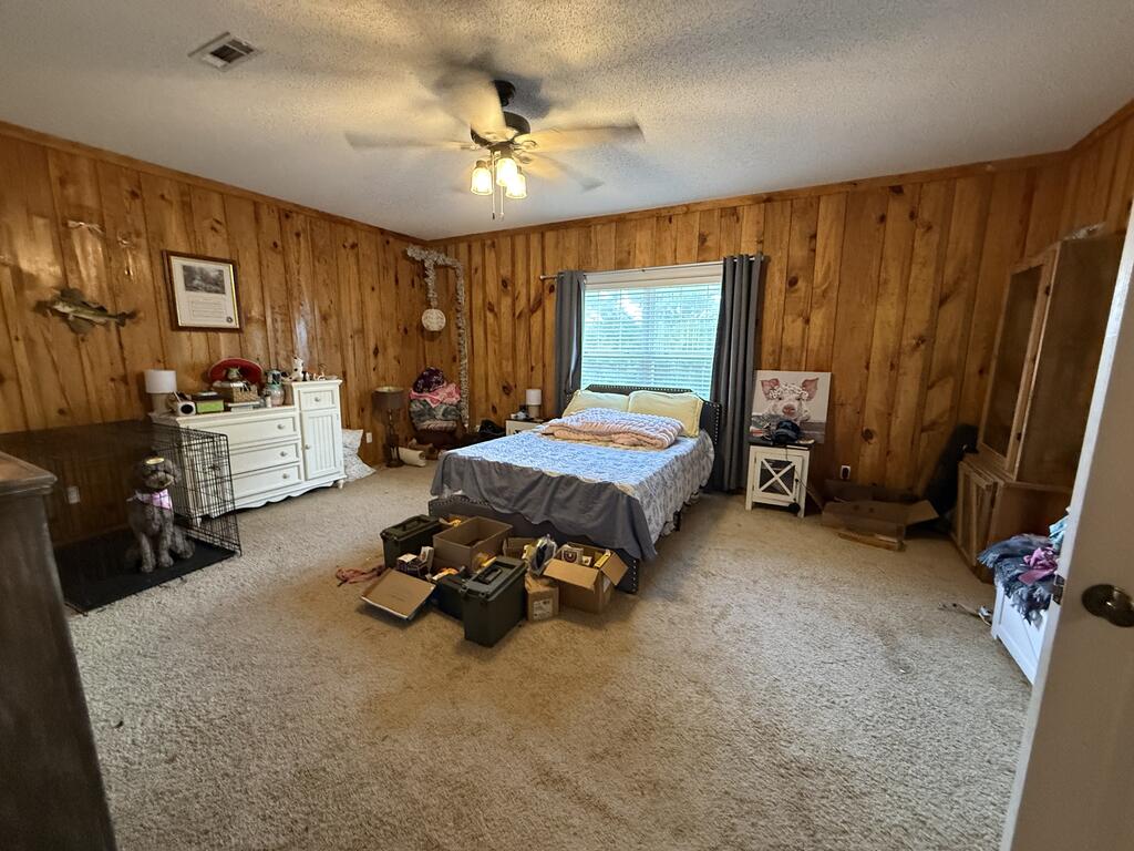 Bedroom with wood-paneled walls, carpet, and a bed beneath a window.