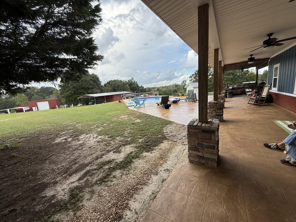 Covered patio overlooking a swimming pool and grassy yard, with ceiling fans and outdoor seating.