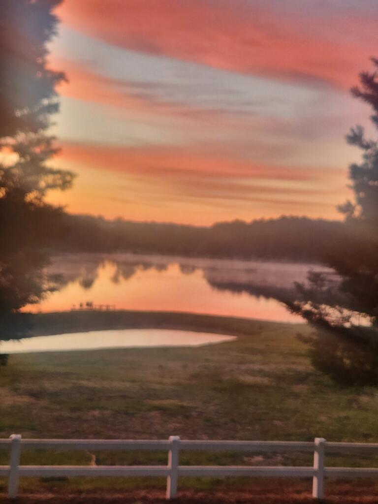 Pond and lake reflect a pink-orange sunset behind a white rail fence.