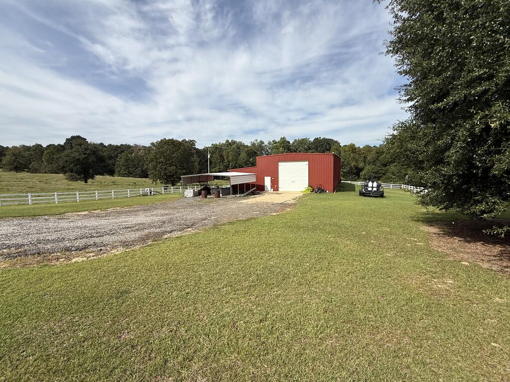 Red metal barn with a white roll-up door beside a gravel drive and fenced pasture.