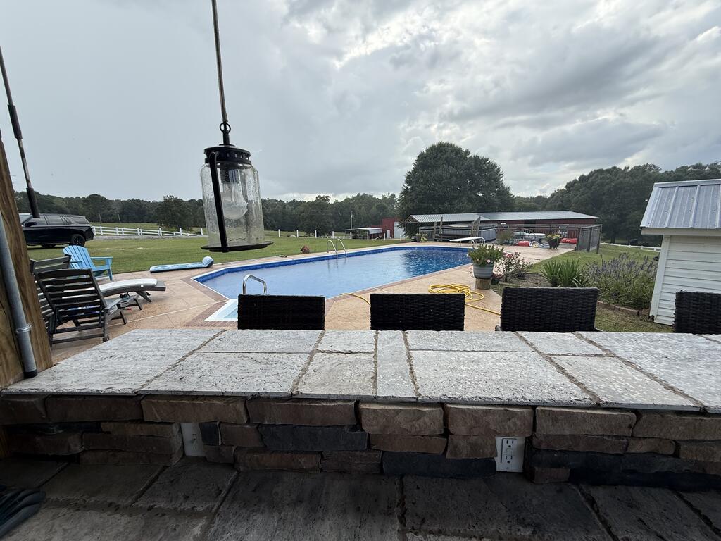 Backyard swimming pool beyond a stone patio counter, with lounge chairs and open lawn.
