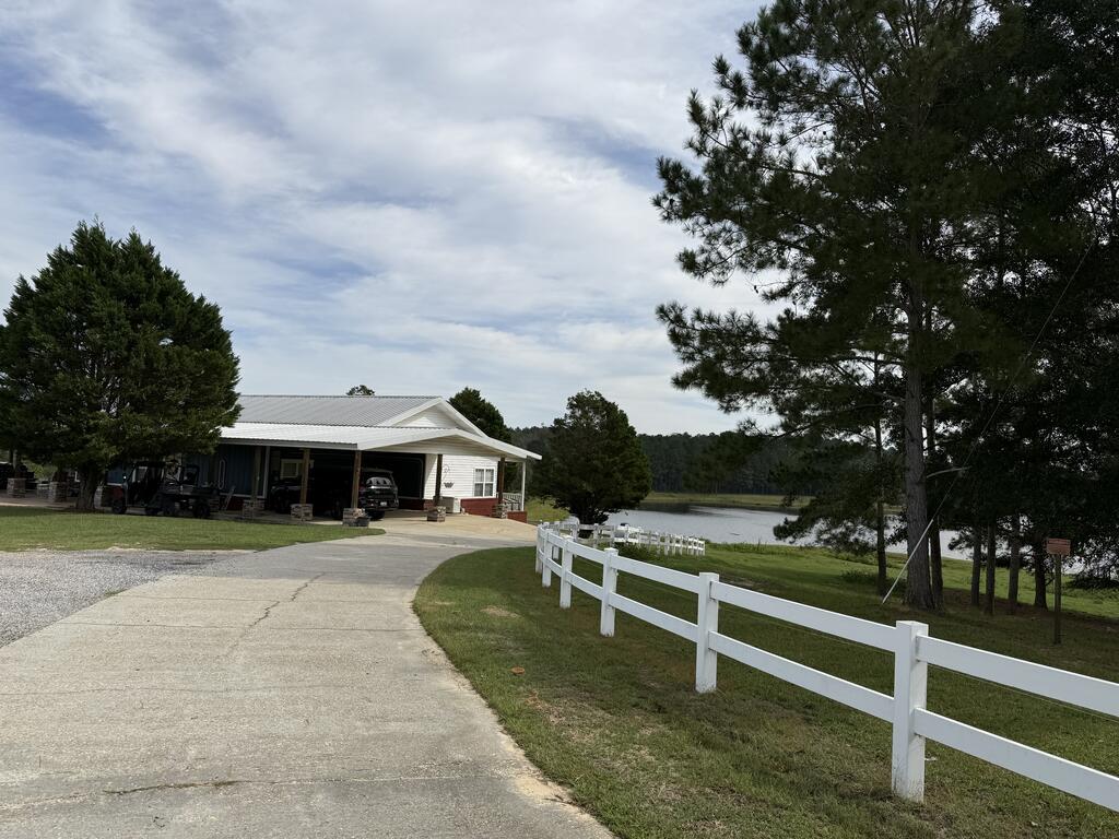 Single-story white property with a covered carport, white fence, and pond beside the driveway.