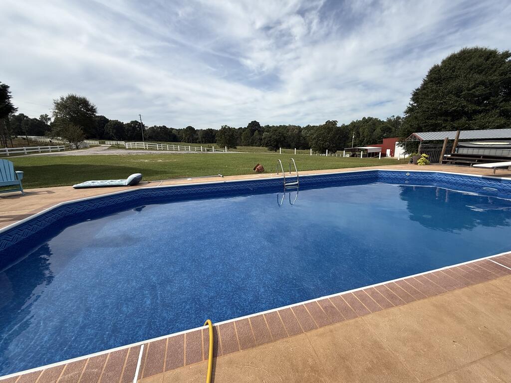 Swimming pool with brick coping and metal ladder beside a wide lawn and white fence.